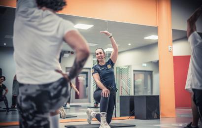 En kvinnlig Fitness24Seven gruppträningsinstruktör visar en rörelse framför en spegel